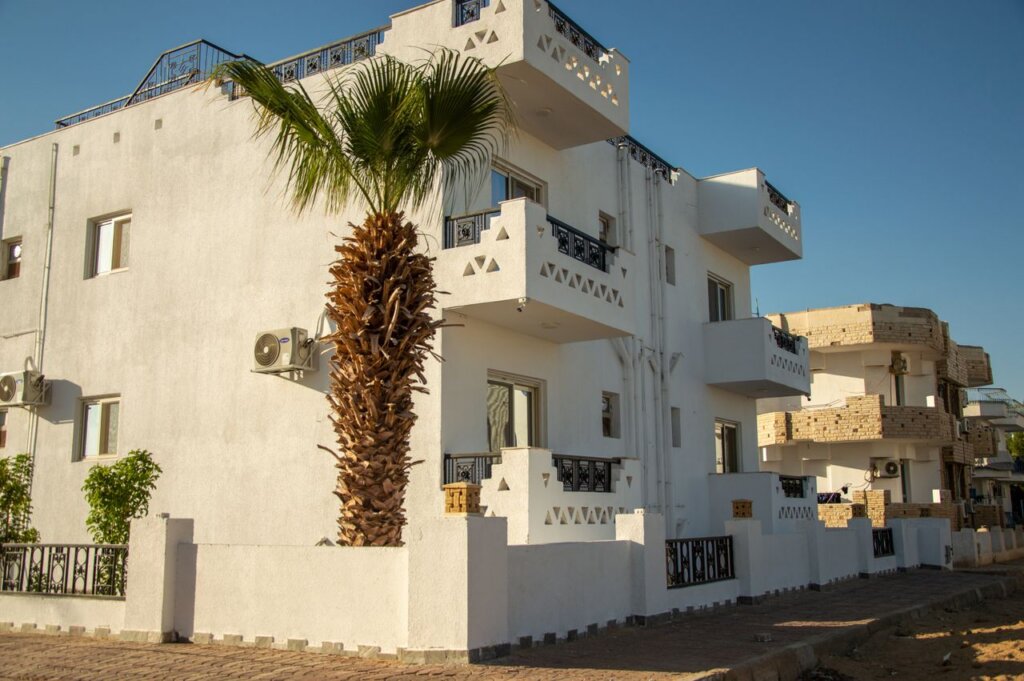 White villa with balconies and palm tree in a sunny residential district.