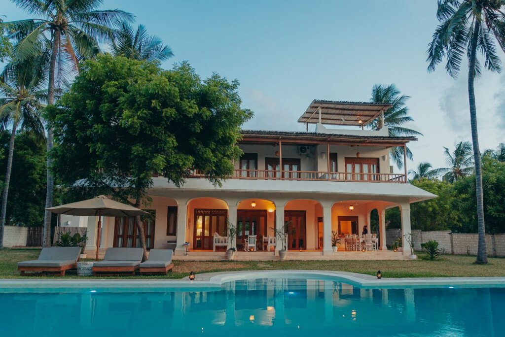 Beautiful tropical villa with a pool surrounded by palm trees at dusk, creating a serene vacation vibe.